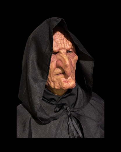 Old Hag silicone witch mask in a black hood, angled front-right view