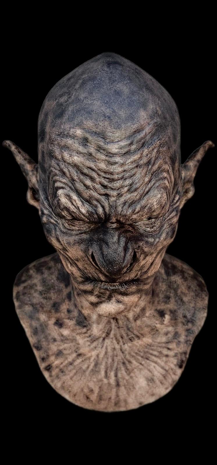 Detailed sculpture of a creature's head with textured skin and large ears on a black background